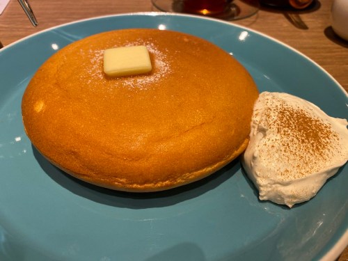 Fluffy pancake topped with a pat of butter, served with a dollop of whipped cream on a blue plate.