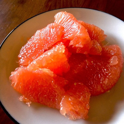 A plate of fresh, juicy pink grapefruit segments arranged neatly.