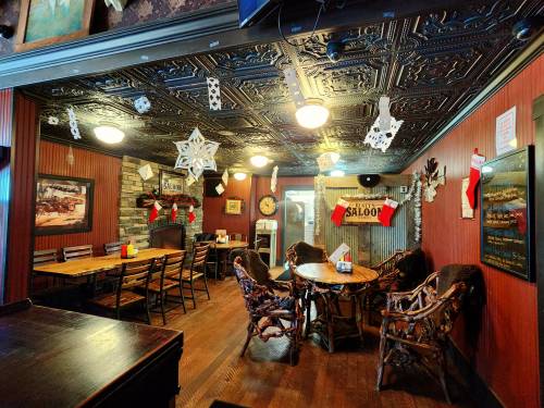 Cozy restaurant interior with wooden tables, chairs, festive decorations, and a stone fireplace.