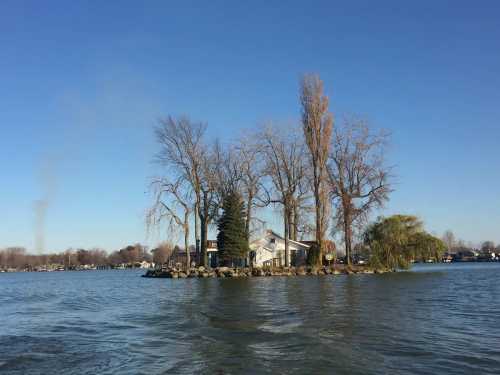 A small island with trees and a house surrounded by calm water under a clear blue sky.