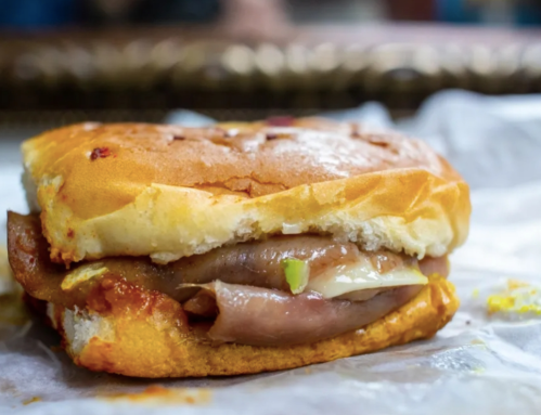 A close-up of a sandwich with layers of meat, sauce, and a soft bun, resting on a piece of parchment paper.
