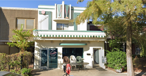 A two-story building with a green and white striped awning, featuring a café entrance and outdoor seating.