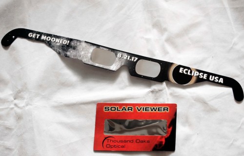 Eclipse glasses with "Get Mooned!" and "Eclipse USA" text, alongside a solar viewer card from Thousand Oaks Optical.