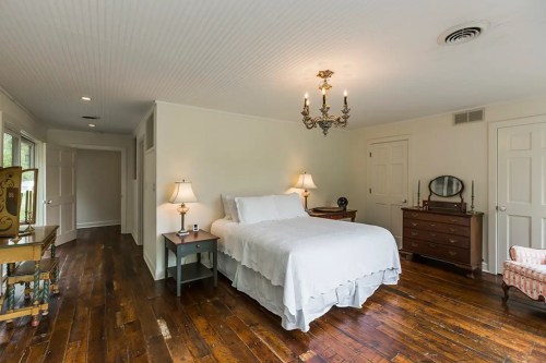 Cozy bedroom with a white bed, wooden floors, a chandelier, and vintage furniture. Soft lighting creates a warm atmosphere.