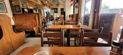 A cozy diner interior with wooden tables and chairs, featuring a counter and a view of patrons in the background.