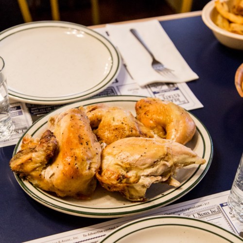 A plate of roasted chicken pieces on a table, with empty plates and glasses in the background.