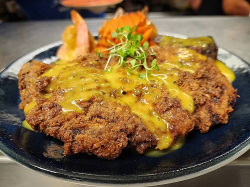 A plate of crispy fried meat topped with a yellow sauce, accompanied by carrots and garnished with fresh herbs.