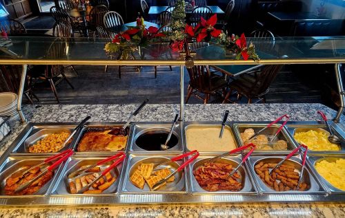 A buffet spread featuring various dishes, including meats, eggs, and sides, with festive decorations in the background.