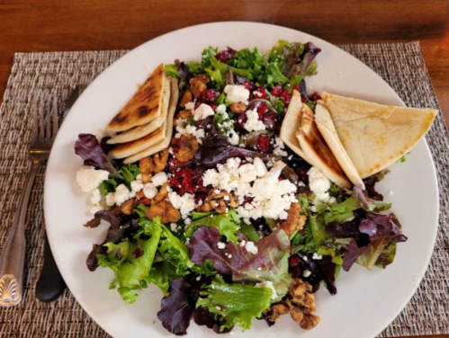 A colorful salad with mixed greens, feta cheese, cranberries, and pita bread on a white plate.