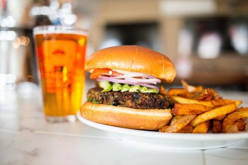 A close-up of a burger with lettuce, tomato, and onion, served with fries and a glass of beer in the background.