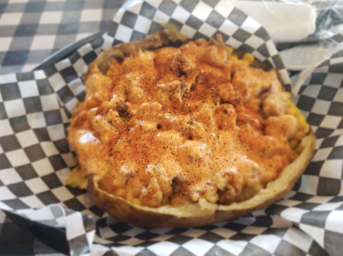 A loaded baked potato topped with cheese, meat, and spices, served in a checkered paper basket.