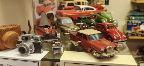 A display of vintage toy cars and a small camera on a shelf, showcasing various classic designs and colors.
