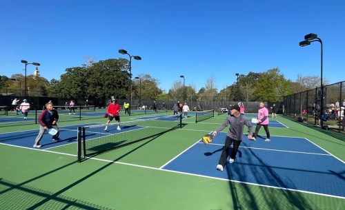 A group of people playing pickleball on outdoor courts under a clear blue sky.