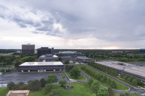Aerial view of a corporate campus with modern buildings, green lawns, and a cloudy sky in the background.