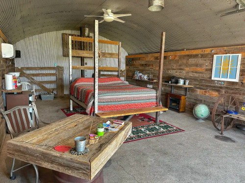 Cozy rustic bedroom with a wooden bed, table, and decor in a corrugated metal room.