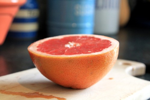 A halved grapefruit on a cutting board, showcasing its pink flesh and textured rind.