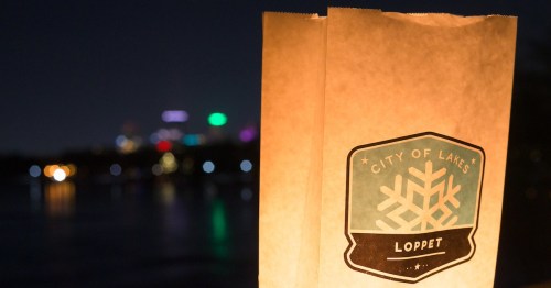 A lit paper lantern with a "City of Lakes Loppet" logo against a blurred night cityscape.