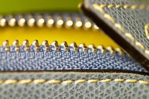 Close-up of a textured zipper with blue fabric and yellow lining, showcasing intricate stitching and details.