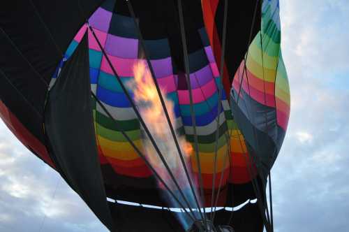 A colorful hot air balloon inflating, with flames visible from the burner against a cloudy sky.