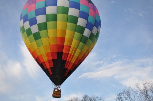 A colorful hot air balloon floats against a blue sky with wispy clouds.