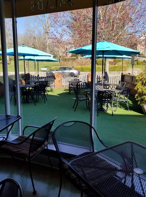 Outdoor seating area with blue umbrellas, green turf, and tables visible through a large window.