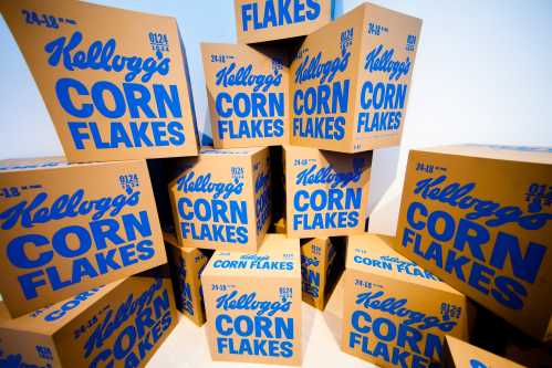 A stack of yellow boxes of Kellogg's Corn Flakes, featuring bold blue text on a light background.