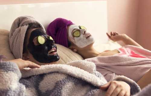 Two people relaxing on a bed with face masks and cucumber slices on their eyes, wearing towels and bathrobes.