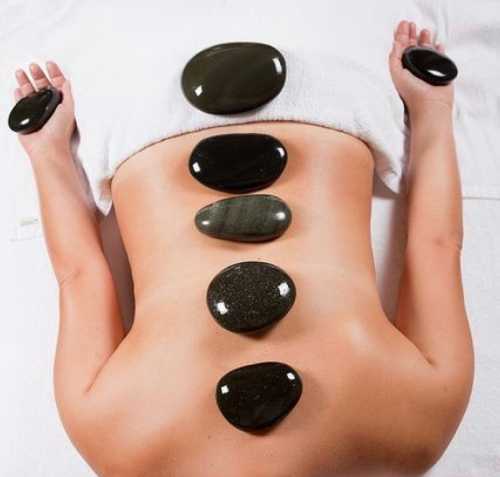 A person lying on a massage table with smooth stones placed along their back for a hot stone therapy treatment.