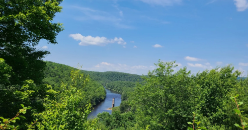 A scenic view of a river winding through lush green hills under a blue sky with fluffy clouds.