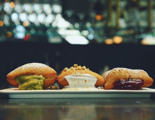 Three filled pastries on a plate: one with green filling, one with white cream, and one with red filling, dusted with powdered sugar.