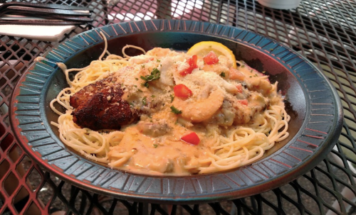 A plate of pasta topped with shrimp, a creamy sauce, and garnished with lemon and herbs, served on a black table.
