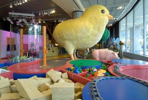 A colorful children's play area featuring large animal sculptures, building blocks, and a train set.
