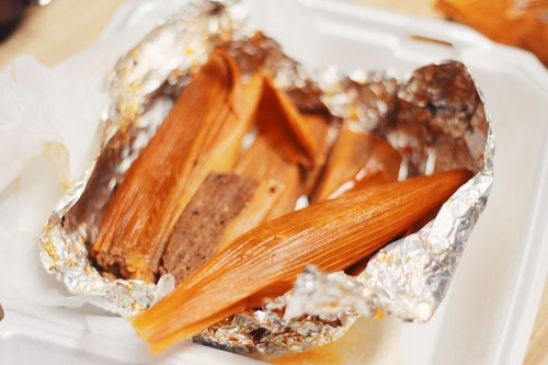 A takeout container with tamales wrapped in corn husks and foil, showcasing their rich, savory filling.
