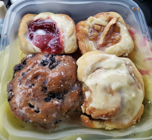 A variety of pastries in a container: a blueberry muffin, cinnamon roll, and two fruit-filled danishes.