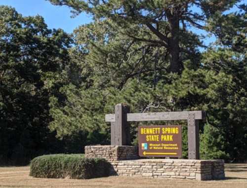 Sign for Bennett Spring State Park, surrounded by trees and grassy area, indicating the park's location in Missouri.
