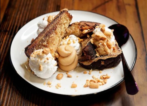 A plate with cake slices topped with whipped cream, peanut butter, and crushed nuts, set on a wooden table.