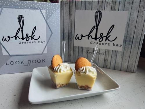 Two dessert cups with whipped cream and a cookie, placed on a plate in front of a "Whisk Dessert Bar" look book.