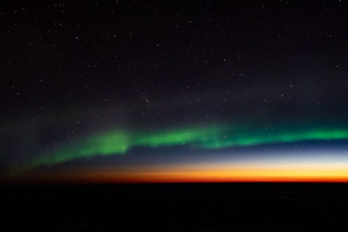 A stunning night sky featuring the aurora borealis with green and blue hues against a starry backdrop and horizon glow.