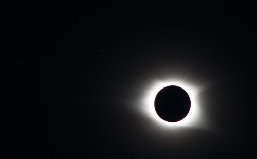 A solar eclipse with a dark moon silhouetted against a bright corona, set against a black sky.