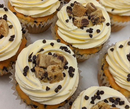 Close-up of cupcakes topped with swirls of frosting, chocolate chips, and cookie dough pieces.