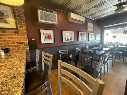 Cozy café interior with wooden floors, black tables, and framed artwork on the walls. Air conditioning units visible.