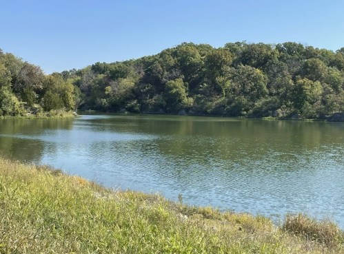 A serene lake surrounded by lush greenery under a clear blue sky.