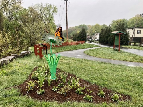 A colorful garden with a butterfly sculpture, surrounded by greenery and a winding path on a rainy day.