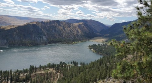 A scenic view of a river winding through mountains, surrounded by lush greenery and a cloudy sky.