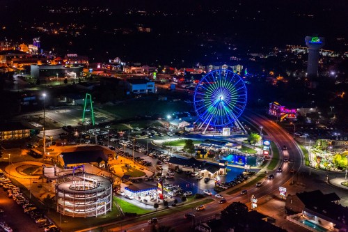 Aerial view of a vibrant amusement park at night, featuring a colorful Ferris wheel and illuminated attractions.