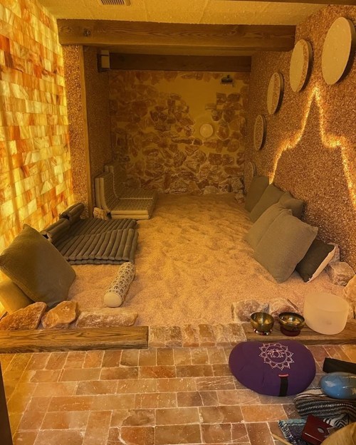A serene salt room with sandy floor, cushions, and soft lighting, designed for relaxation and wellness.