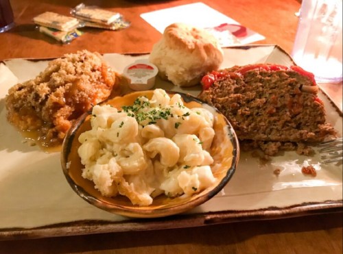 A plate with meatloaf, macaroni and cheese, a biscuit, and a side of peach cobbler.