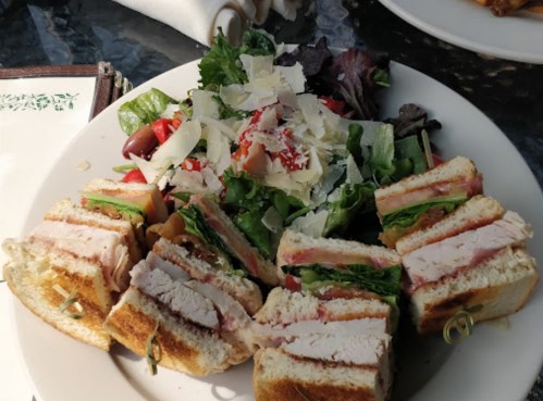 A plate with a sliced sandwich stacked with turkey, lettuce, and tomato, accompanied by a fresh salad with parmesan.
