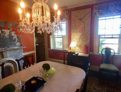 A bright dining room with a chandelier, orange walls, a patterned wallpaper, and a table set with decorative items.