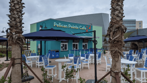 Exterior of Pelican Pointe Café with outdoor seating, palm trees, and a cloudy sky in the background.